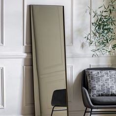 a mirror sitting next to a chair and a plant in a room with white walls