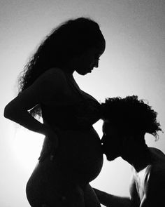 a pregnant woman standing next to a man in front of the sun with her hands on her hips