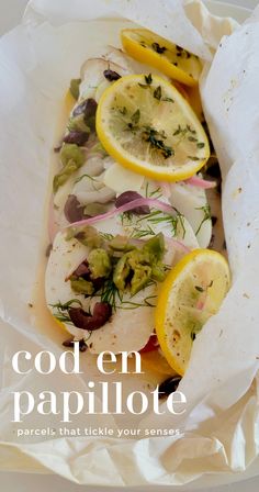 a white plate topped with fish covered in lemons and herbs on top of parchment paper