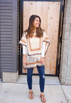 a woman standing in front of a wooden door wearing sandals and a sweater over her shoulders