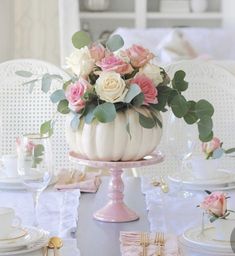 a white pumpkin decorated with pink roses and greenery sits on a table set for an elegant tea party