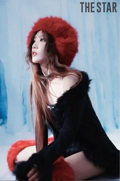 a woman with long hair wearing a red hat and black fur coat sitting on the ground