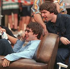 two young men sitting on top of a brown leather chair next to each other in front of a crowd