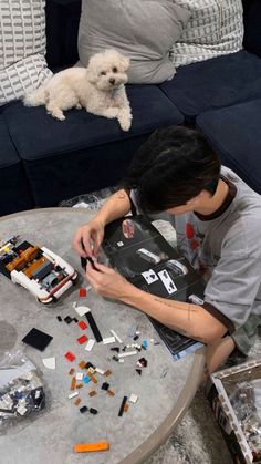 a person sitting at a table with legos on it and a dog laying in the background