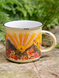 a coffee mug with flowers painted on it sitting on a rock in front of some plants