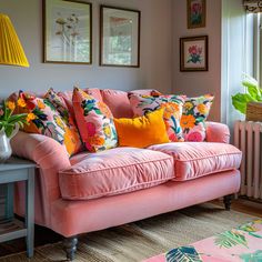 a pink couch with colorful pillows on top of it in front of a radiator