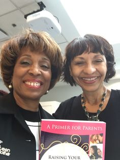 two women standing next to each other with a book in front of their faces and smiling