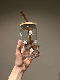 a hand holding a glass with a straw in it and flowers painted on the inside