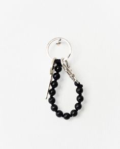 a black beaded keychain hanging from a metal hook on a white background