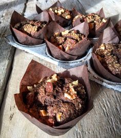 several muffins sitting on top of each other in paper wrappers next to a wooden table