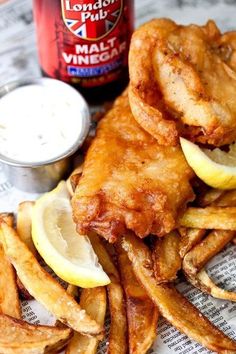 fish and chips with lemon wedges next to a can of beer