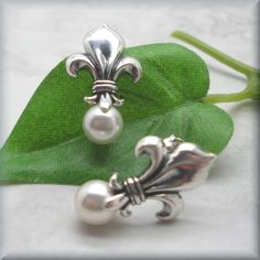 "Sterling silver fleur de lis stud earrings are accented with a glowing white Swarovski elements half-drilled pearl. Classic, beautiful and unusual. This symbol has traditionally been used to represent French royalty, and in that sense it is said to signify perfection, light, and life. Fleur de lis translates to \"flower of the lily\" in English. The earrings are about 7/8\" long (1.8 cm) from the top of the fleur de lis to the bottom of the pearl. Setting, earnuts and earring components are all Elegant Silver Flower Clip-on Earrings, Classic White Flower Earrings For Pierced Ears, White Classic Flower Earrings For Pierced Ears, Classic White Flower Earrings, White Classic Flower Earrings, Elegant Silver Clip-on Flower Earrings, Classic White Flower Earrings For Formal Occasions, Classic Silver Flower Earrings For Wedding, Classic White Sterling Silver Clip-on Earrings