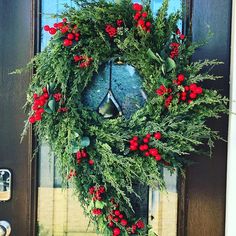 a wreath is hanging on the front door with red berries and greenery around it