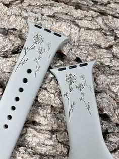 two white watch bands with flowers on them sitting next to each other in front of a rock