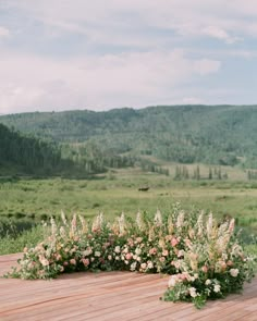 an outdoor ceremony setup with flowers and greenery on the ground in front of mountains