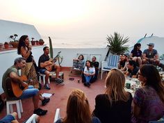 a group of people sitting on top of a roof next to the ocean playing guitar