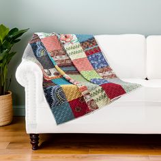 a white couch with a multicolored quilt on it and a potted plant in the corner