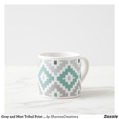 a white and green patterned cup sitting on top of a marble counter next to a wall