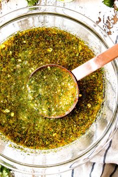 a wooden spoon in a glass bowl filled with pesto and seasoning on a table