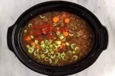 a black crock pot filled with soup and vegetables