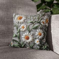 a pillow with white daisies on it sitting on a gray couch next to a plant