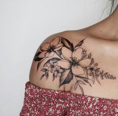 a woman's shoulder with flowers and leaves tattooed on the back of her shoulder