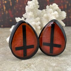 pair of red and black earrings with cross cut out on the sides, sitting next to white flowers