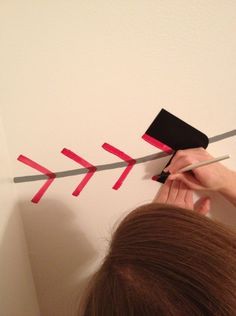 a woman is painting a wall with red tape and black stick on the top of it