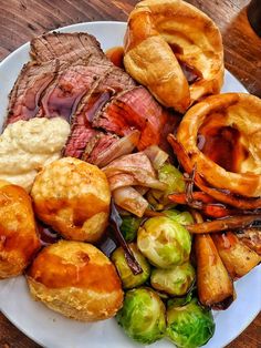 a white plate topped with meat, potatoes and brussel sprouts on top of a wooden table