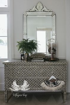 a white and black dresser with a mirror on it's sideboard next to a potted plant