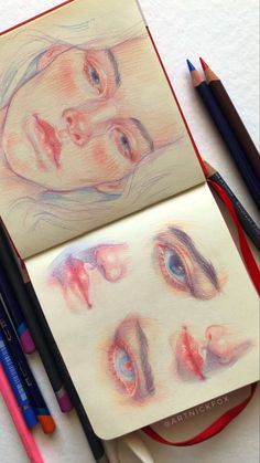 colored pencils next to an open notebook with drawings of two women's faces