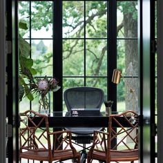 two chairs and a desk in front of a large window with plants on the table