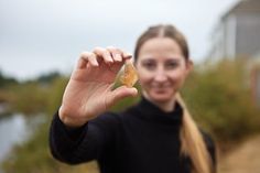 a woman holding up a piece of food in her hand while standing next to a body of water