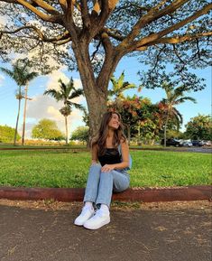 a woman sitting under a tree on the side of a road with her legs crossed