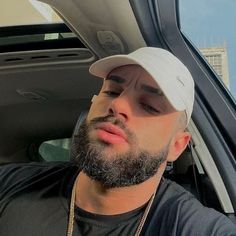 a man with a beard wearing a white hat and looking out the back window of a car