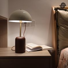 a table lamp sitting on top of a wooden desk next to a book and pillow