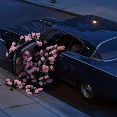 an old car parked on the side of the road with flowers growing out of it