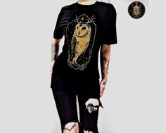 🦉 Stolas, the Owl Demon on on a super-soft 100% jet-black cotton t-shirt 🦉 **All of the designs are my original artworks.This particular design is being directly screen-printed with ecological water-based inks :) ** 👕THE MATERIAL: 100 %  ringspun ORGANIC cotton!  THE FIT: Unisex fit. THE COLOR of the print: WHITE or GOLDEN (matte/no shimmer)  🤗 CARE INSTRUCTIONS :  Please always wash your t-shirt with cold water  Avoid dryers and strong laundry detergents / softeners 🚚 THE SHIPPING I always Black Fairy Grunge Crew Neck Top, Black Crew Neck Fairy Grunge Top, Fitted Black T-shirt In Fairy Grunge Style, Black Gothic T-shirt For Fall, Fairy Grunge Black Halloween Top, Black Fairy Grunge Tops For Halloween, Black Fairy Grunge Top For Streetwear, Black Fairy Grunge T-shirt For Streetwear, Fairy Grunge Black T-shirt For Halloween