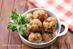 meatballs with parsley in a white bowl on a wooden table next to a red and white checkered napkin