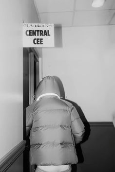 black and white photograph of a person in a coat entering a room with a central cee sign on the wall