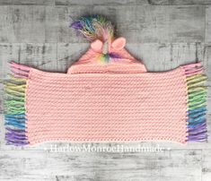 a pink crocheted baby blanket with multicolored fringes on the sides