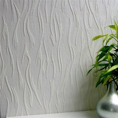 a green plant in a silver vase next to a white wallpapered with wavy lines