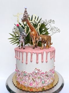 there is a cake decorated with animals and flowers on the top, along with palm leaves