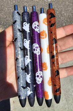 four different colored pens with skulls and pumpkins on them are in the palm of someone's hand