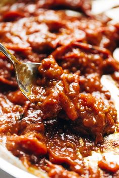 a spoon is being used to scoop sauce out of a white bowl filled with meat