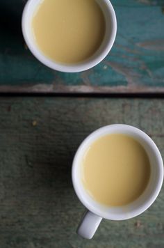 two mugs of coffee sitting on top of a wooden table next to each other