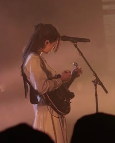 a woman holding a guitar while standing in front of a microphone