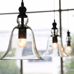 three glass bell lights hanging from a ceiling in front of a window with large windows