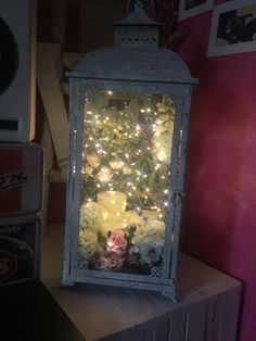 a lighted lantern sitting on top of a wooden table next to a box filled with flowers