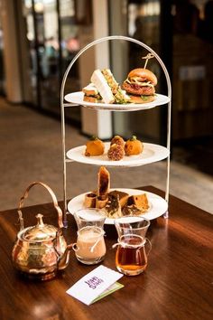 three tiered trays holding sandwiches and tea on a wooden table in a restaurant